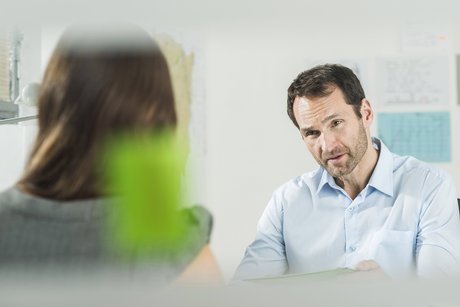 Ein Mann und eine Frau in förmlicher Kleidung sitzen sich gegenüber, die Situation sieht aus wie ein Vorstellungsgespräch