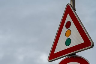 Ein Verkehrsschild "Achtung Ampel" vor wolkengrauem Himmel