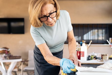 Eine ältere Frau mit Gummihandschuhen wischt einen Bilderrahmen ab.