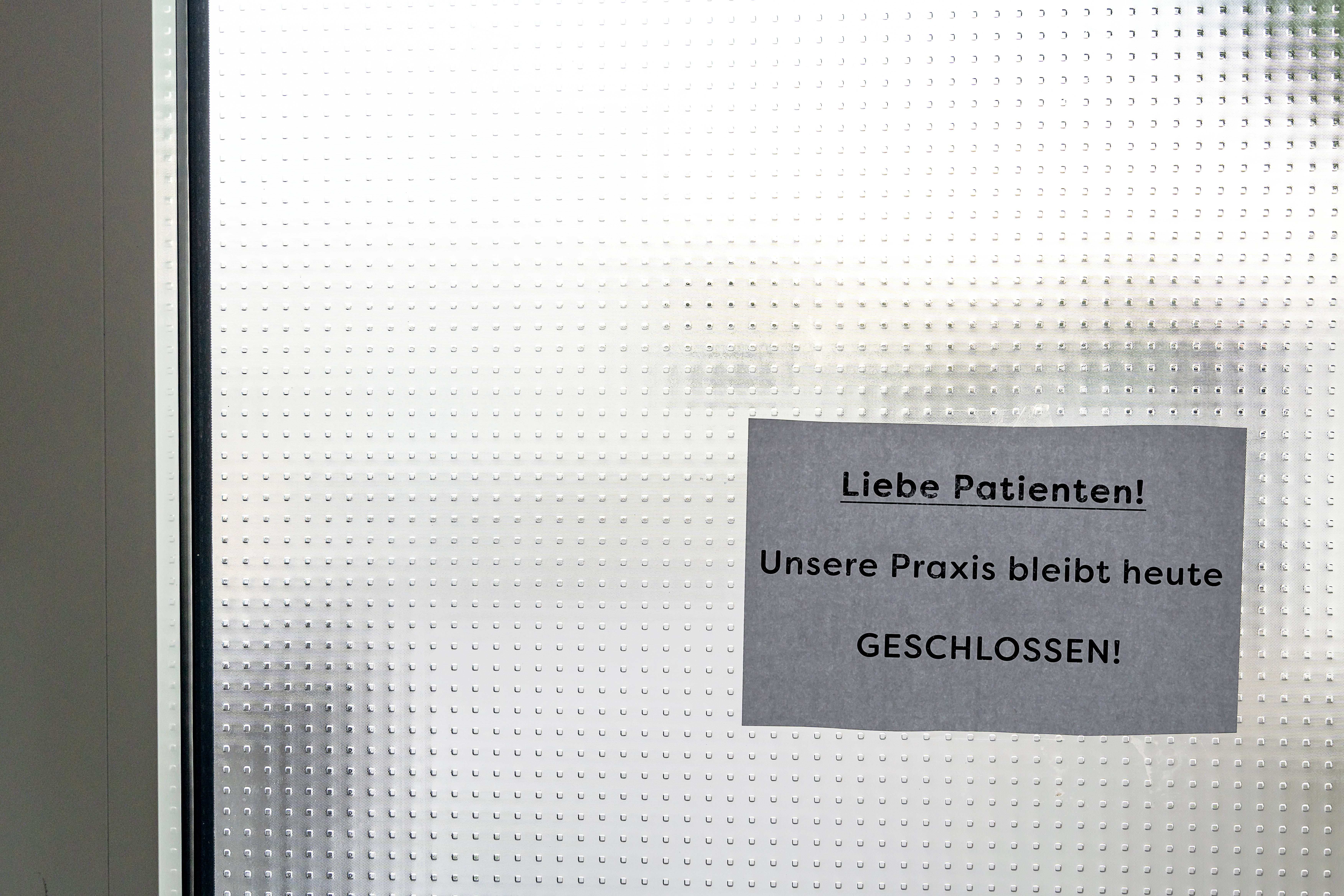 Eine Glastür, an der ein ausgedruckter Zettel hängt mit der Aufschrift "Liebe Patienten! Unsere Praxis bleibt heute geschlossen."