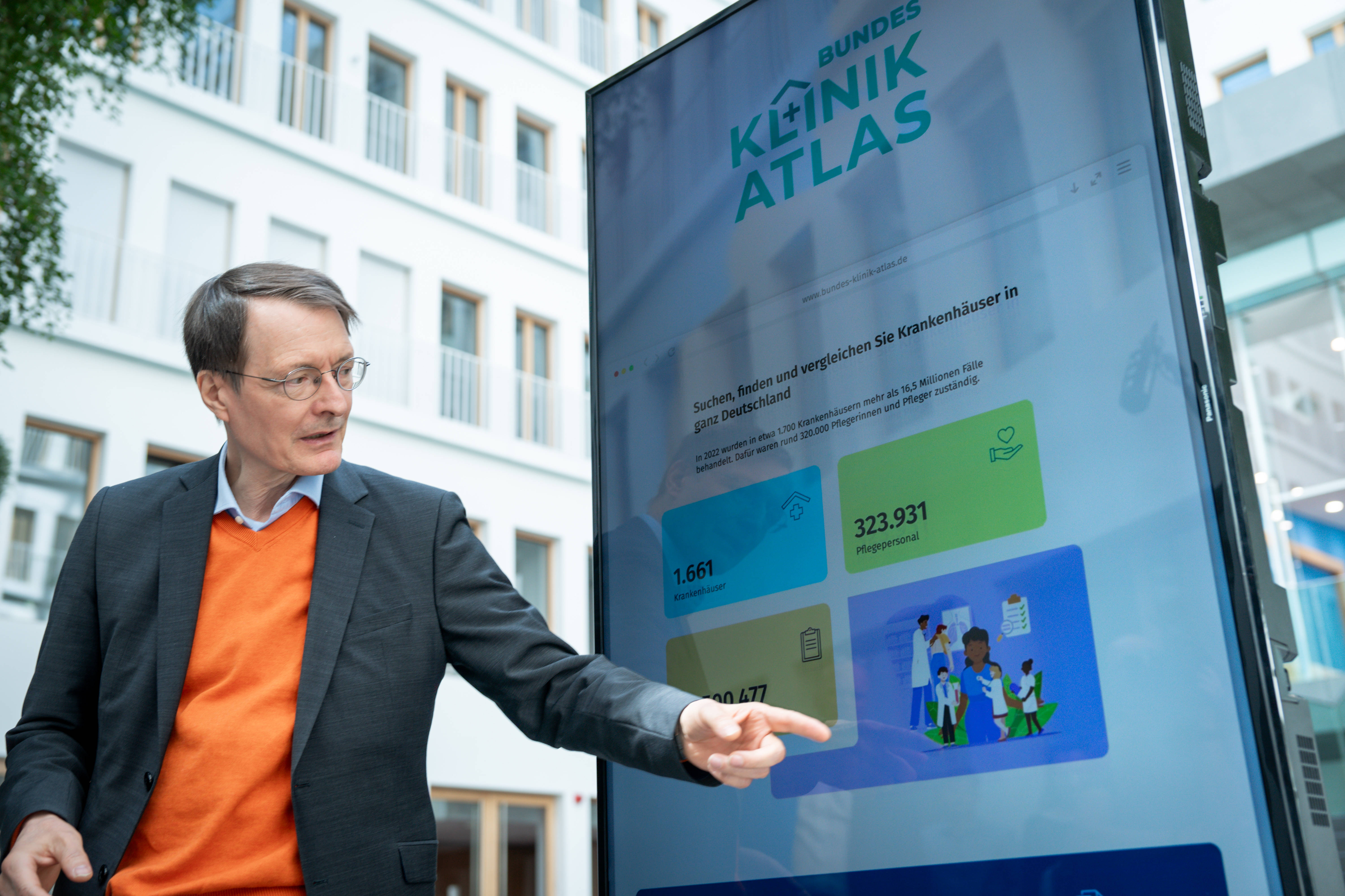 Karl Lauterbach steht vor einem Display und zeigt auf Grafiken des neuen Klinik-Atlas